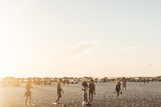 A beach scene with people enjoying a sunny day outdoors, featuring umbrellas and a bright atmosphere.