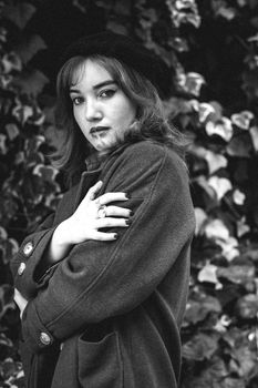 Elegant woman in vintage coat poses with ivy backdrop. Timeless black and white portrait.