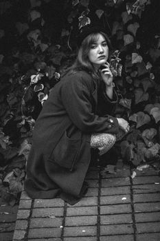 Black and white portrait of a woman crouched outdoors against leafy background.