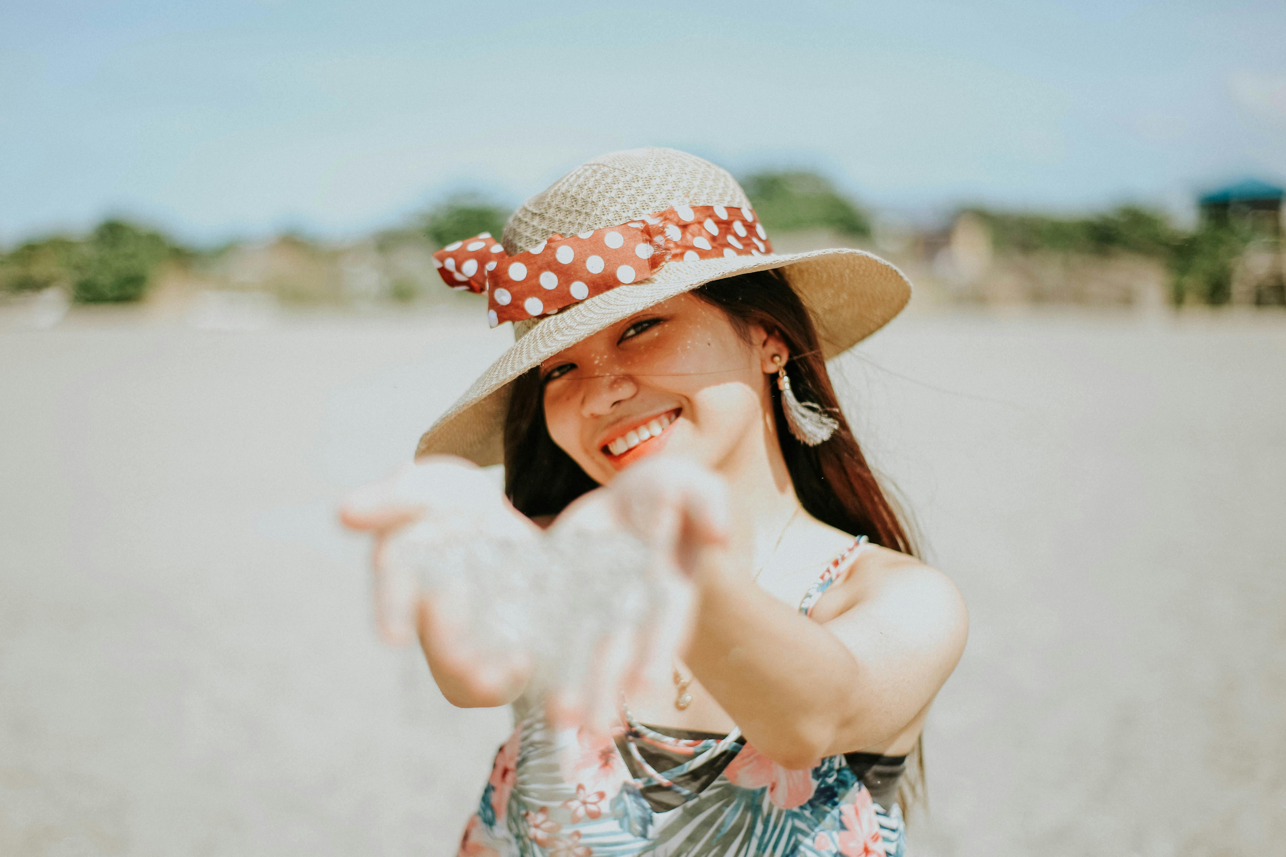 Free Asian woman smiling in sun hat enjoys a sunny day on the beach, radiating joy and relaxation. Stock Photo