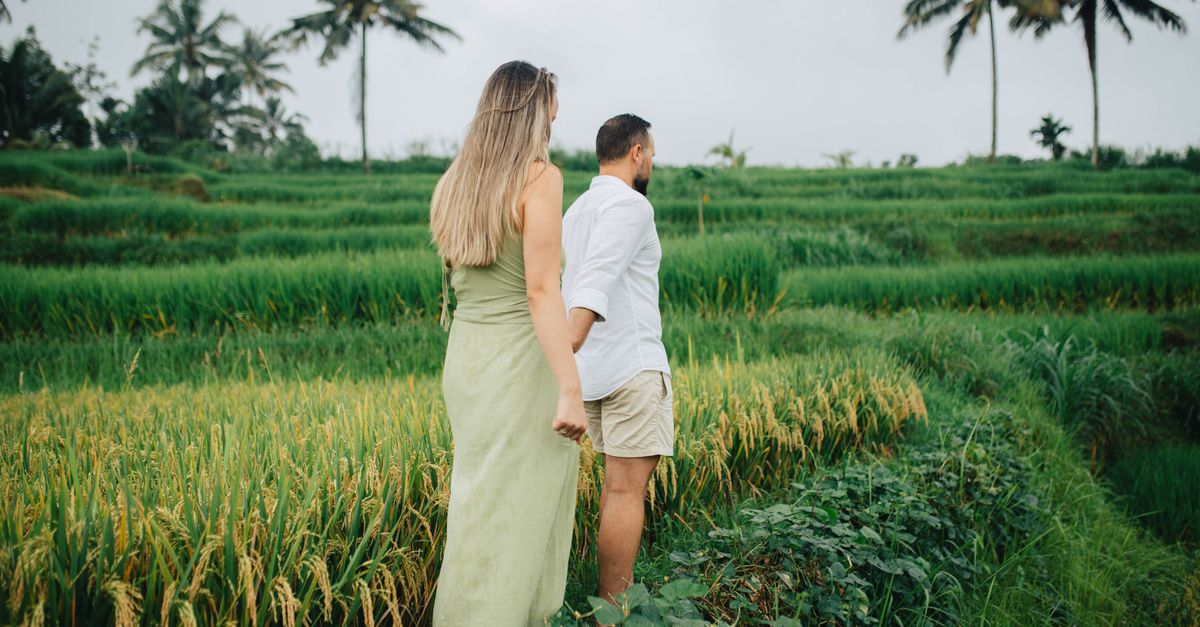 Couple walking among lush Balinese rice terraces holding hands, capturing serenity and nature.