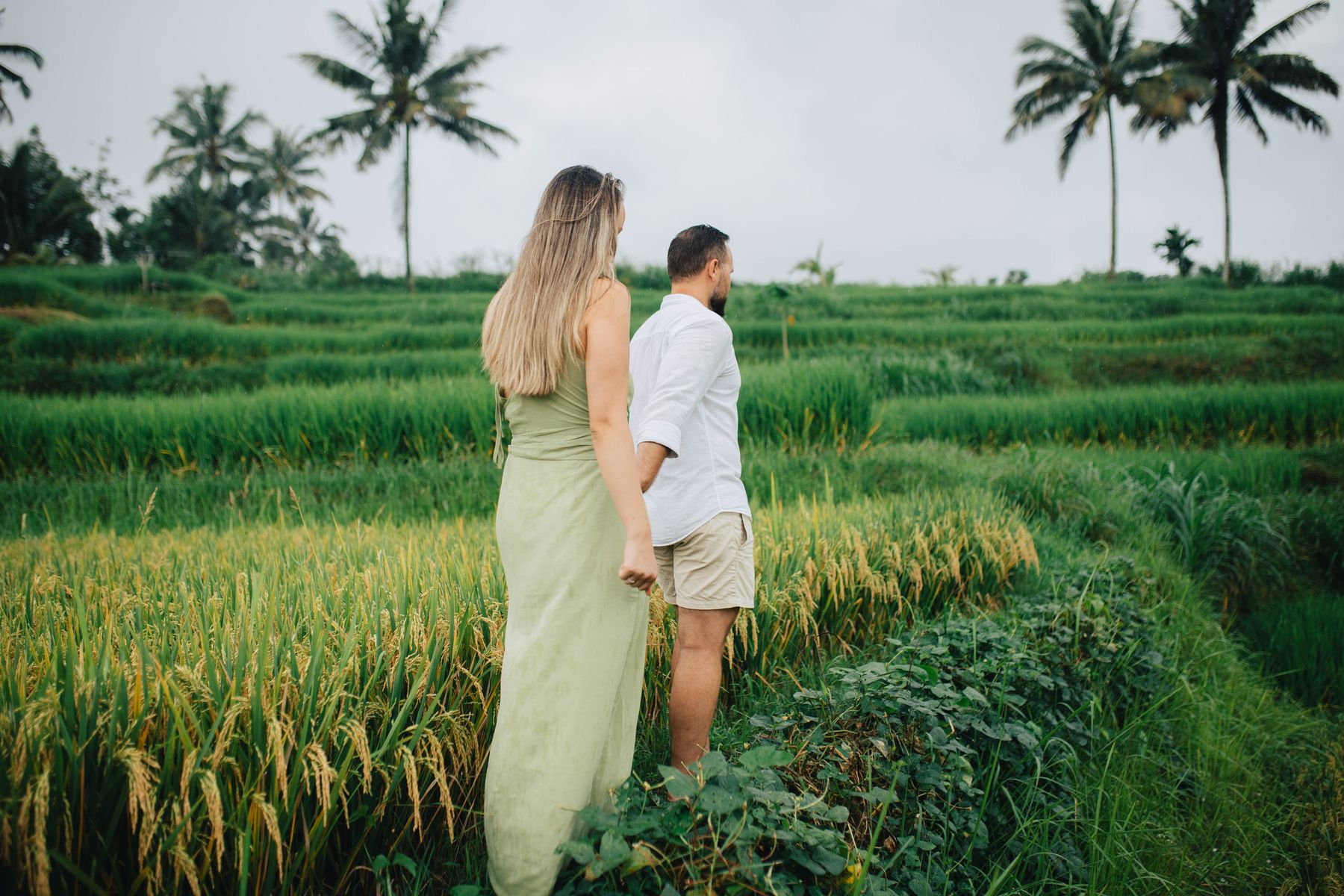 Couple walking together through layered Balinese rice terraces and palms