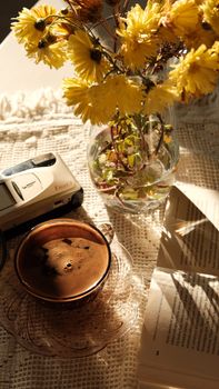 Warm sunlit scene with coffee, flowers, and book. Perfect for relaxing moments.