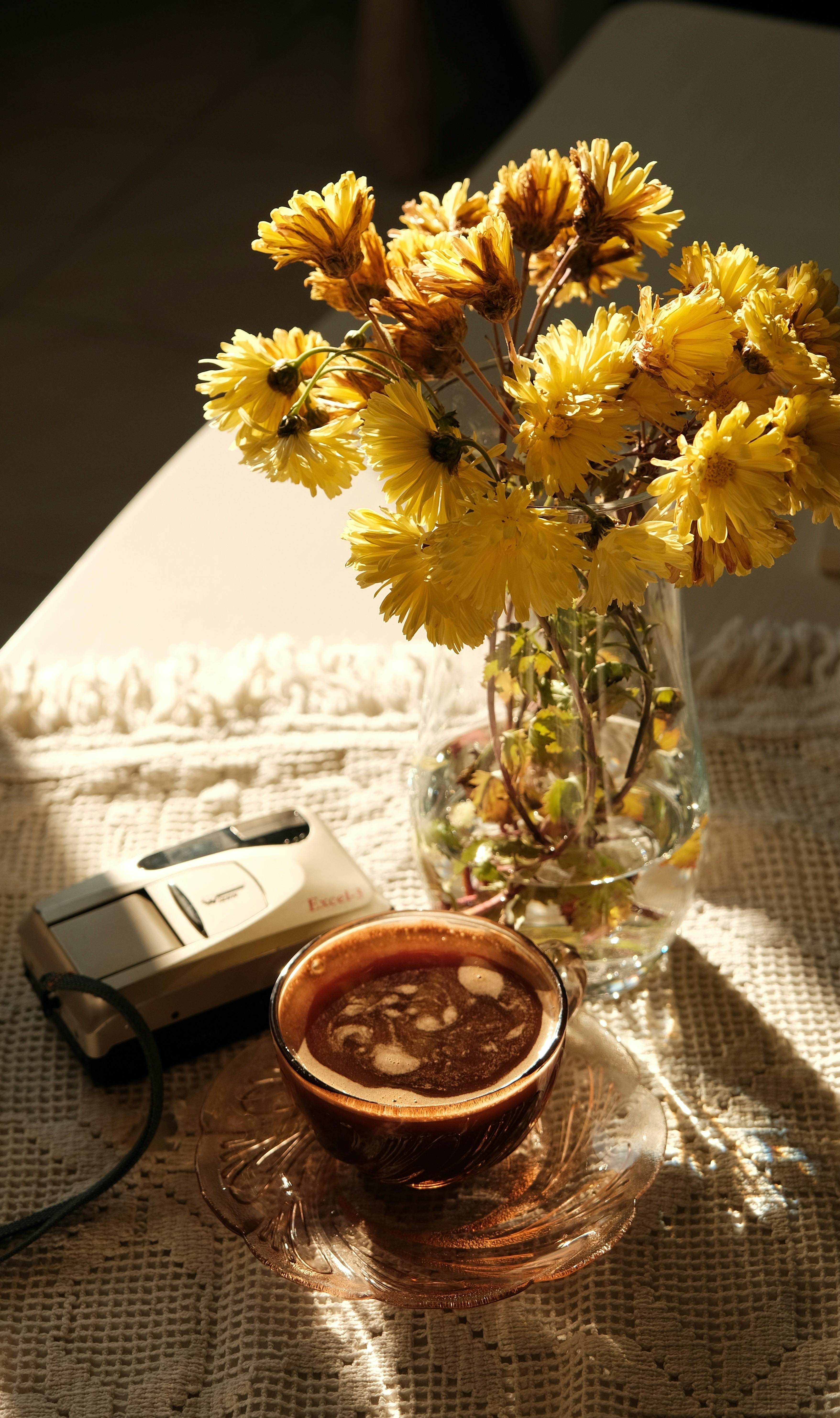 Warm still life with coffee, yellow flowers, and retro camera in soft sunlight.