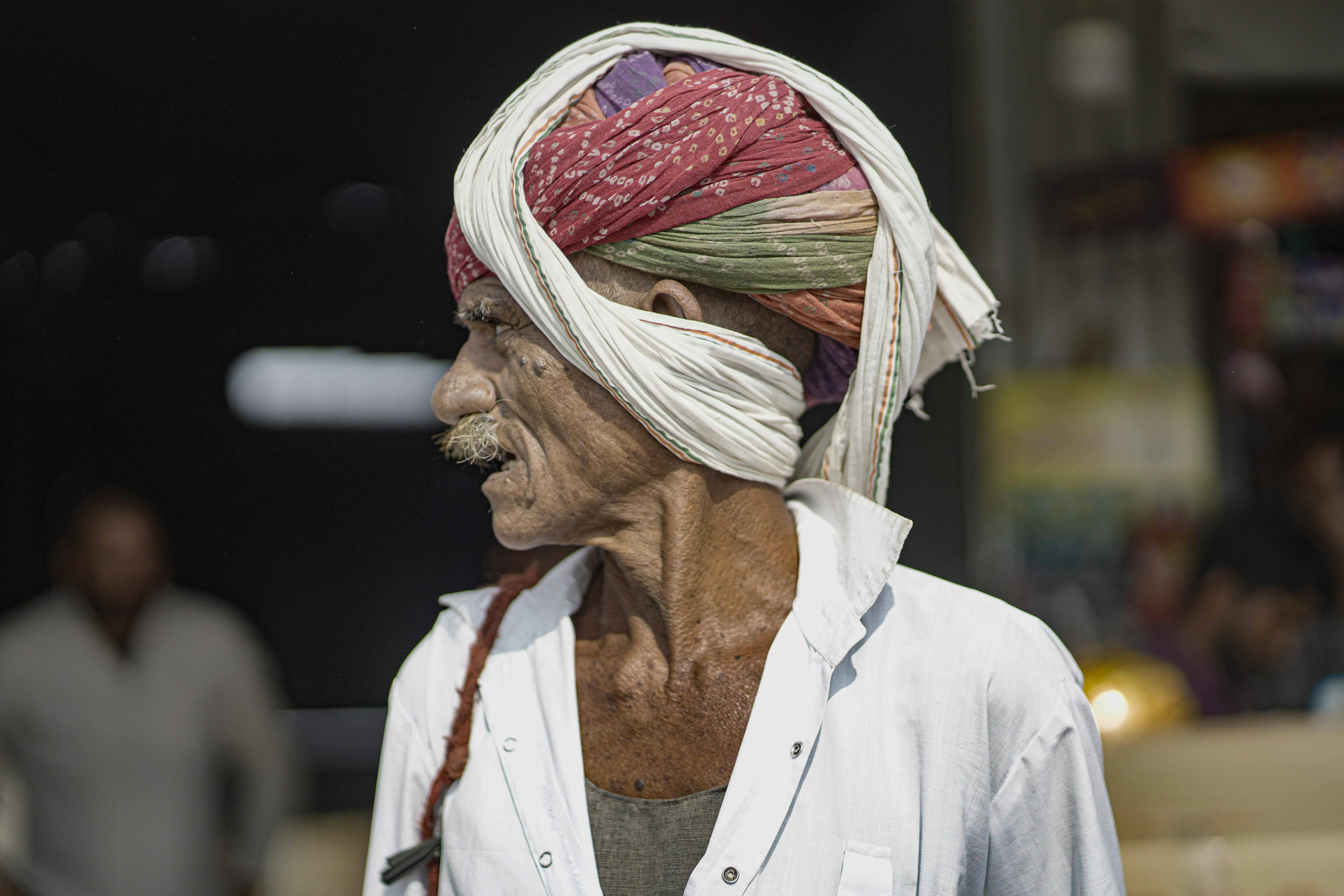 Elderly Rajasthani man with colorful turban and white attire, outdoors in India.