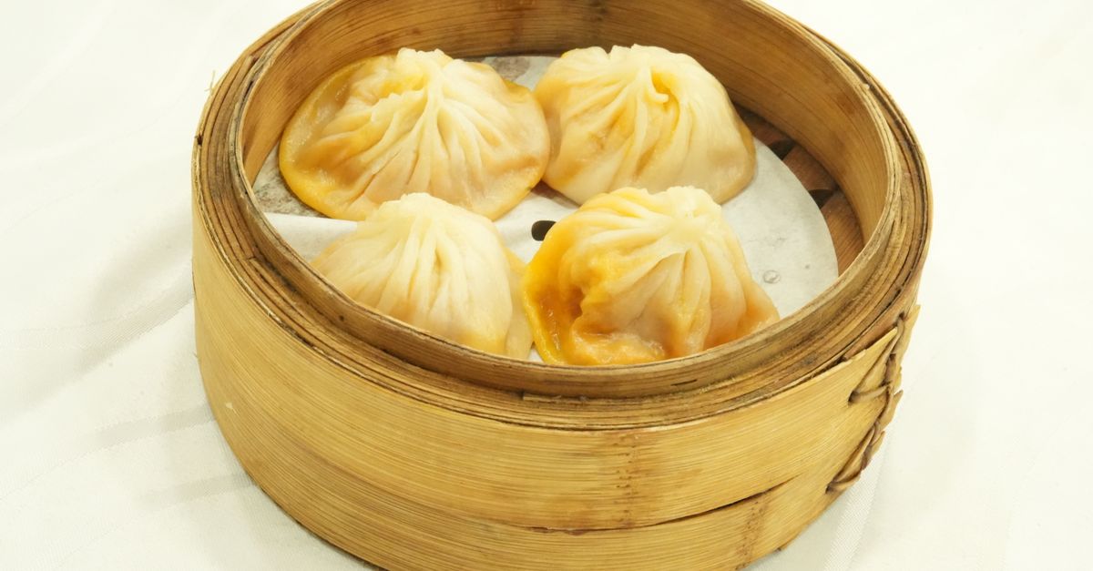 Gros plan de raviolis vapeur dans un panier en bambou sur fond blanc, parfait pour les thèmes liés à la cuisine asiatique.
