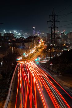 Vibrant night view of a city street with light trails and illuminated skyline in the distance.