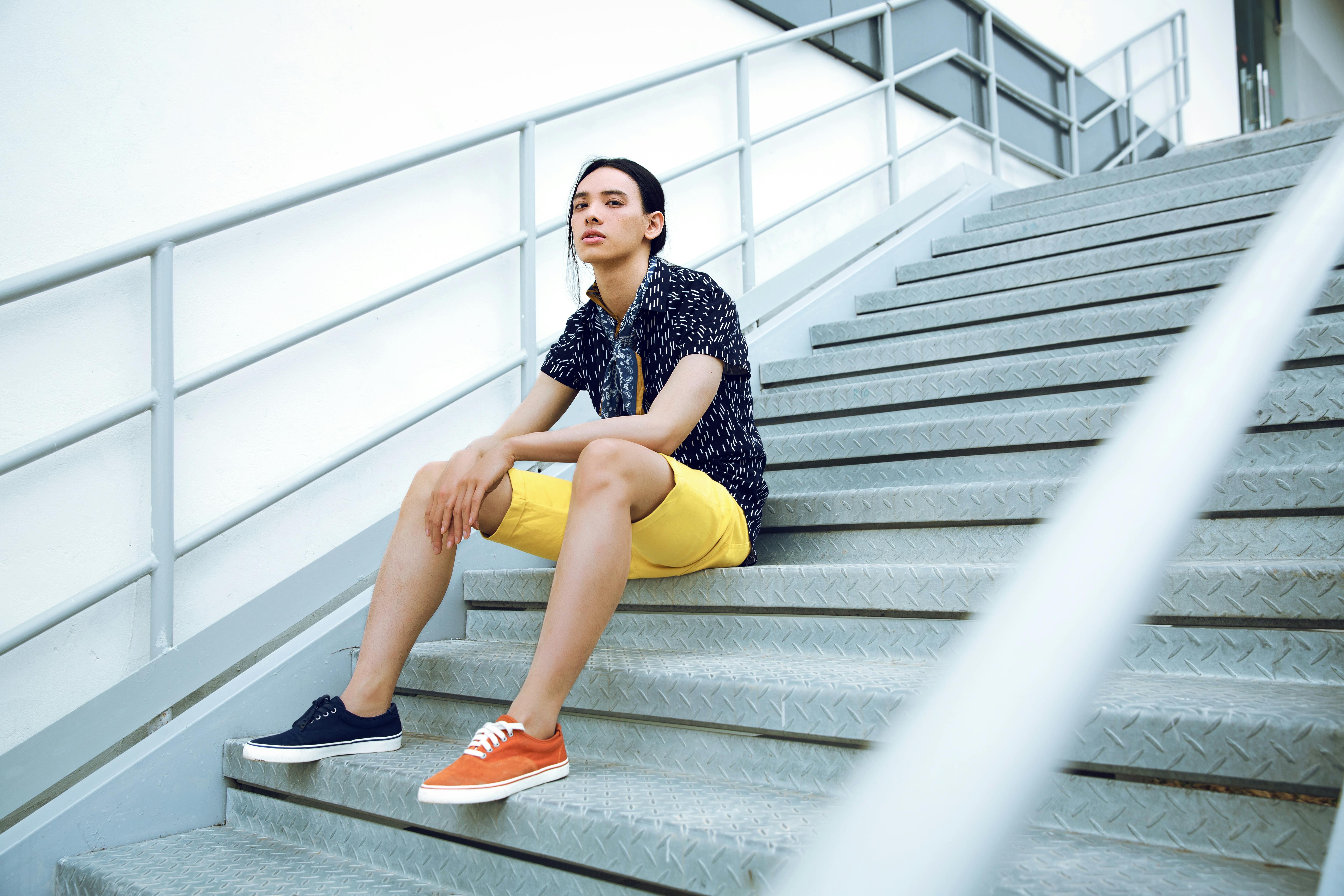 Young adult seated on industrial stairs wearing vibrant summer fashion.