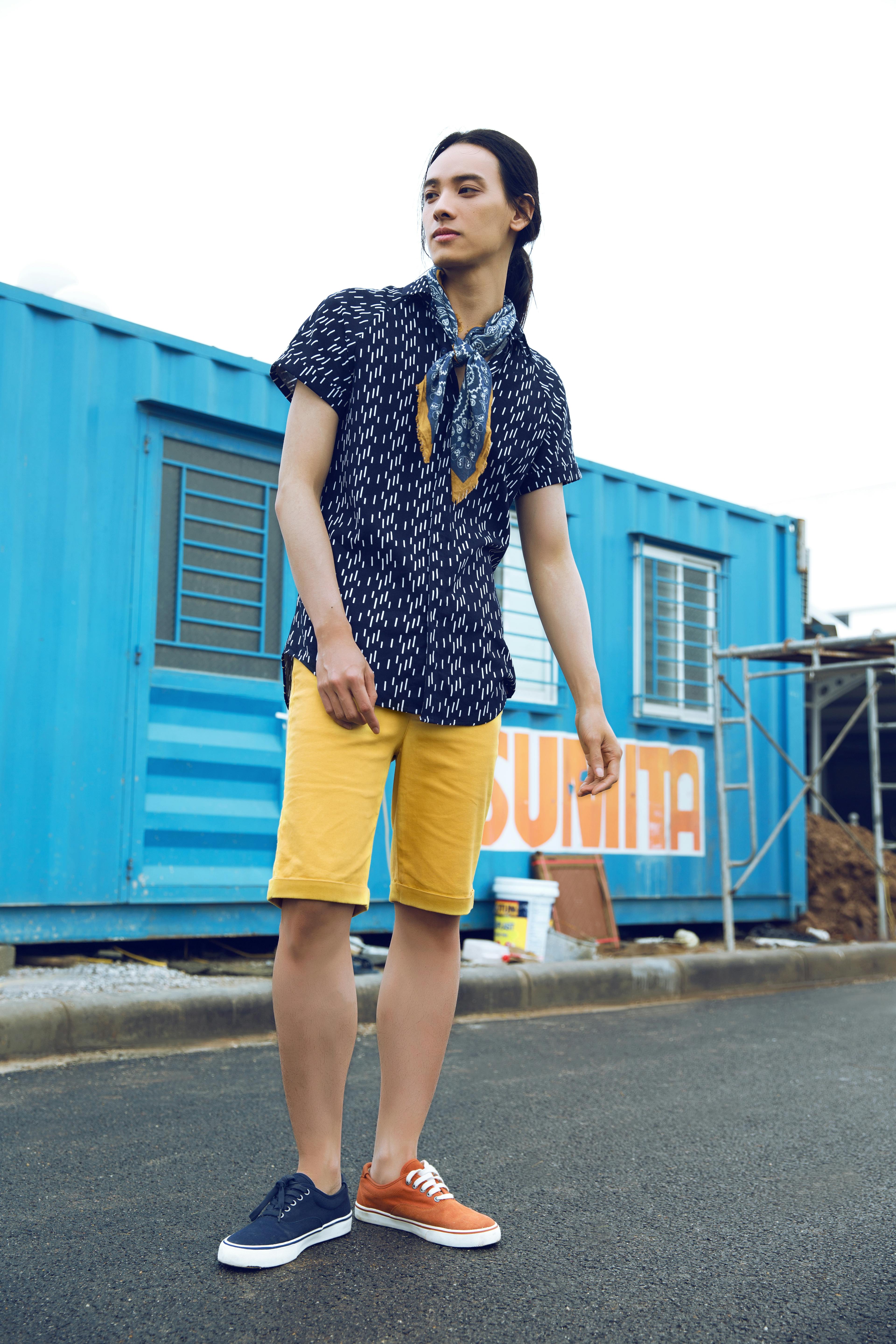 Young adult in stylish outfit standing near blue container outdoors.