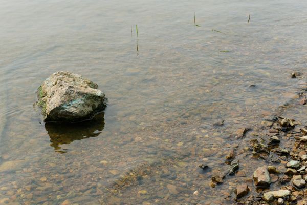 Rocher isolé dans une eau claire et peu profonde sur une rive de galets