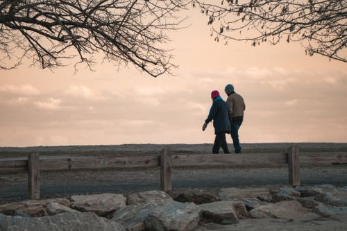Free A senior couple strolls along a scenic park path under a colorful autumn sky. Stock Photo