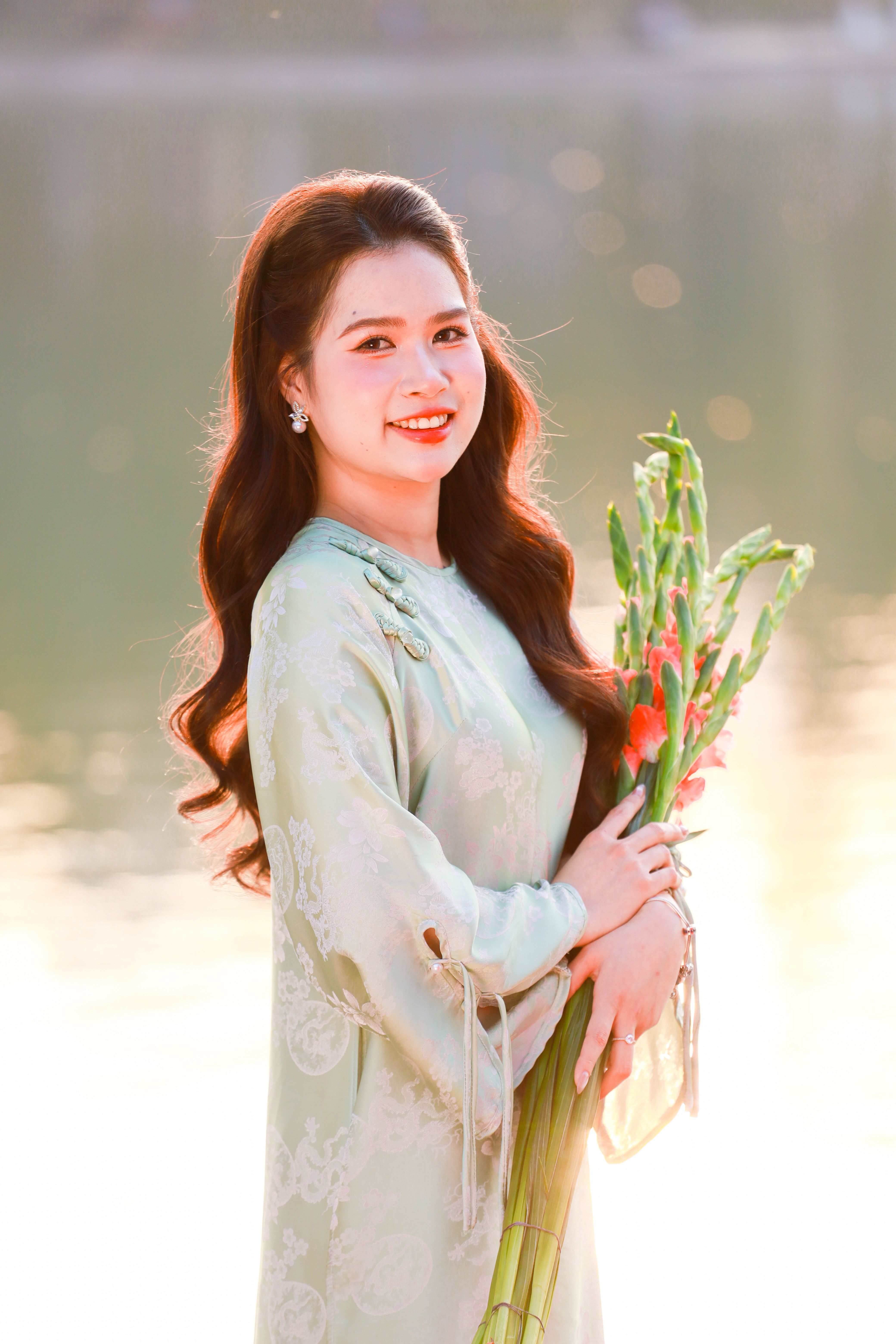 Vietnamese woman in traditional áo dài holding flowers by a serene lake in Hanoi.