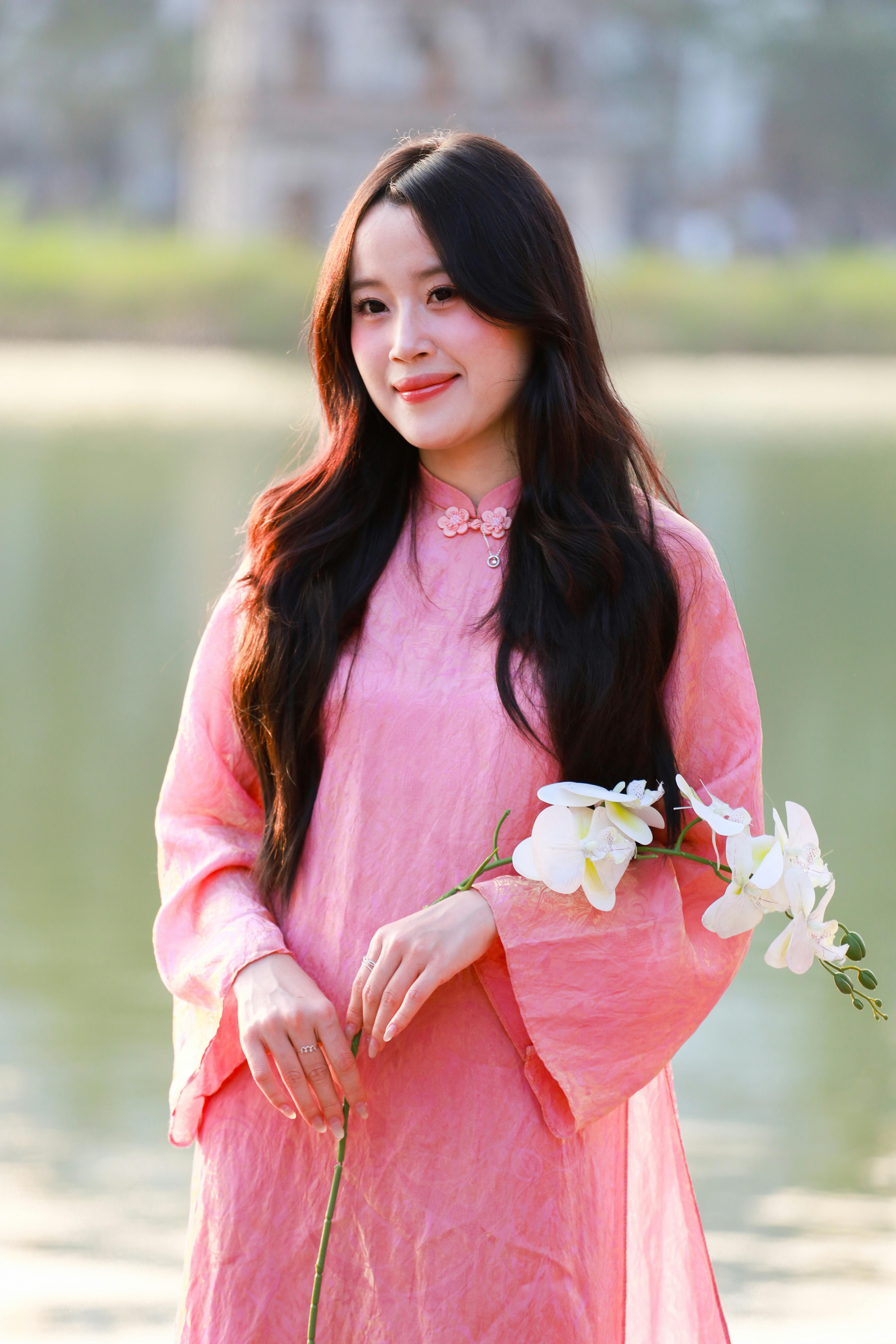 Portrait of a woman in pink Ao Dai holding flowers by a lake in Hanoi, Vietnam.