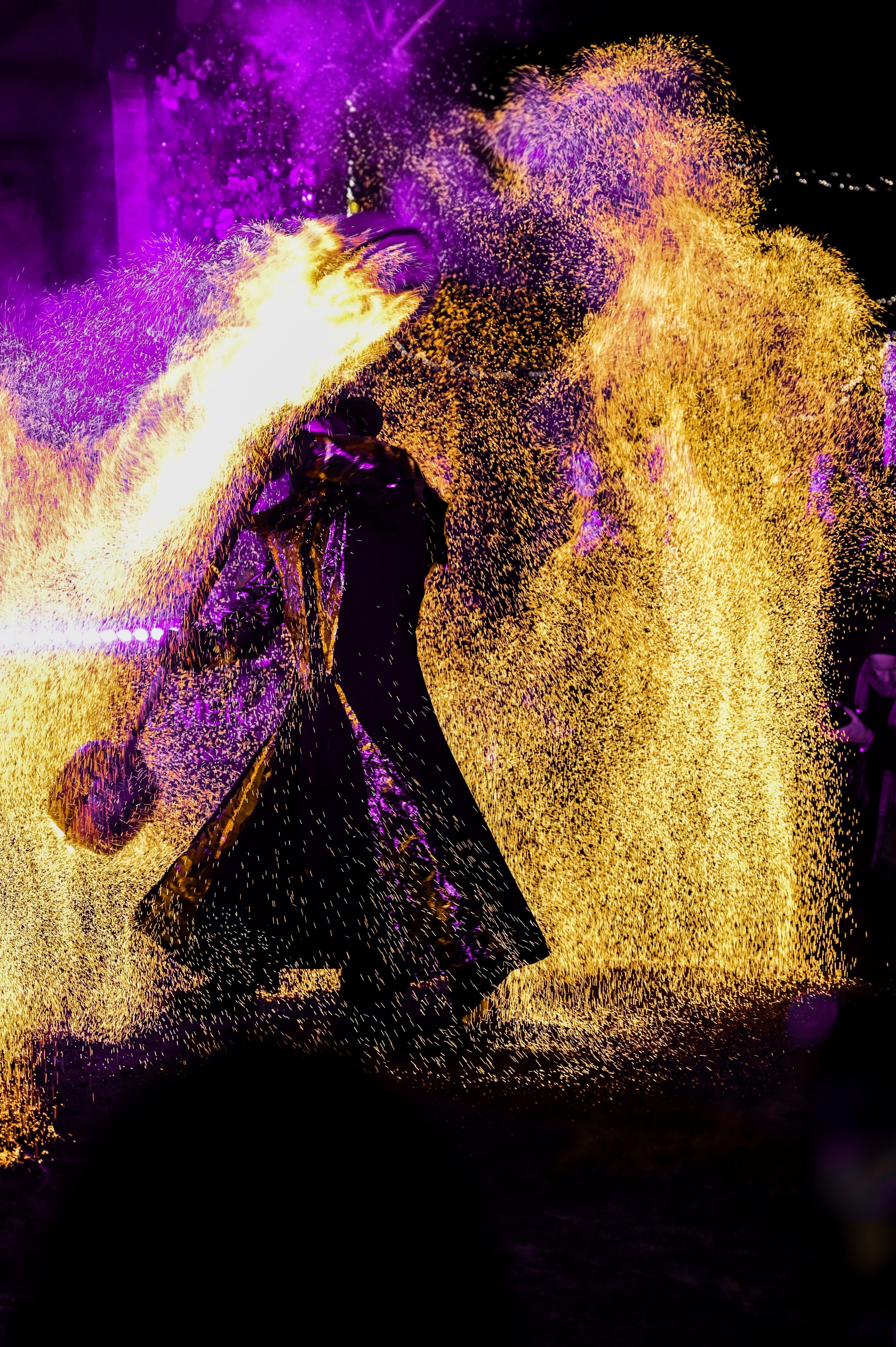 Dazzling fire performer spinning flames with vivid colors at night event.