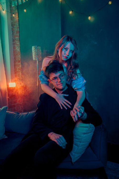 Free A couple enjoys a quiet moment in a moody, warmly lit living room setting. Stock Photo