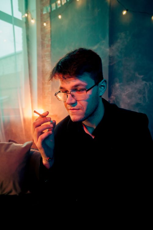 Free Young man smoking indoors with soft lighting and smoke creating a moody atmosphere. Stock Photo