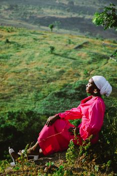 Portrait of an African woman in a pink dress enjoying a serene outdoor view.