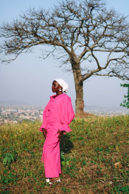 Elegant woman in vibrant pink dress posing outdoors with a scenic view in Abuja, Nigeria.