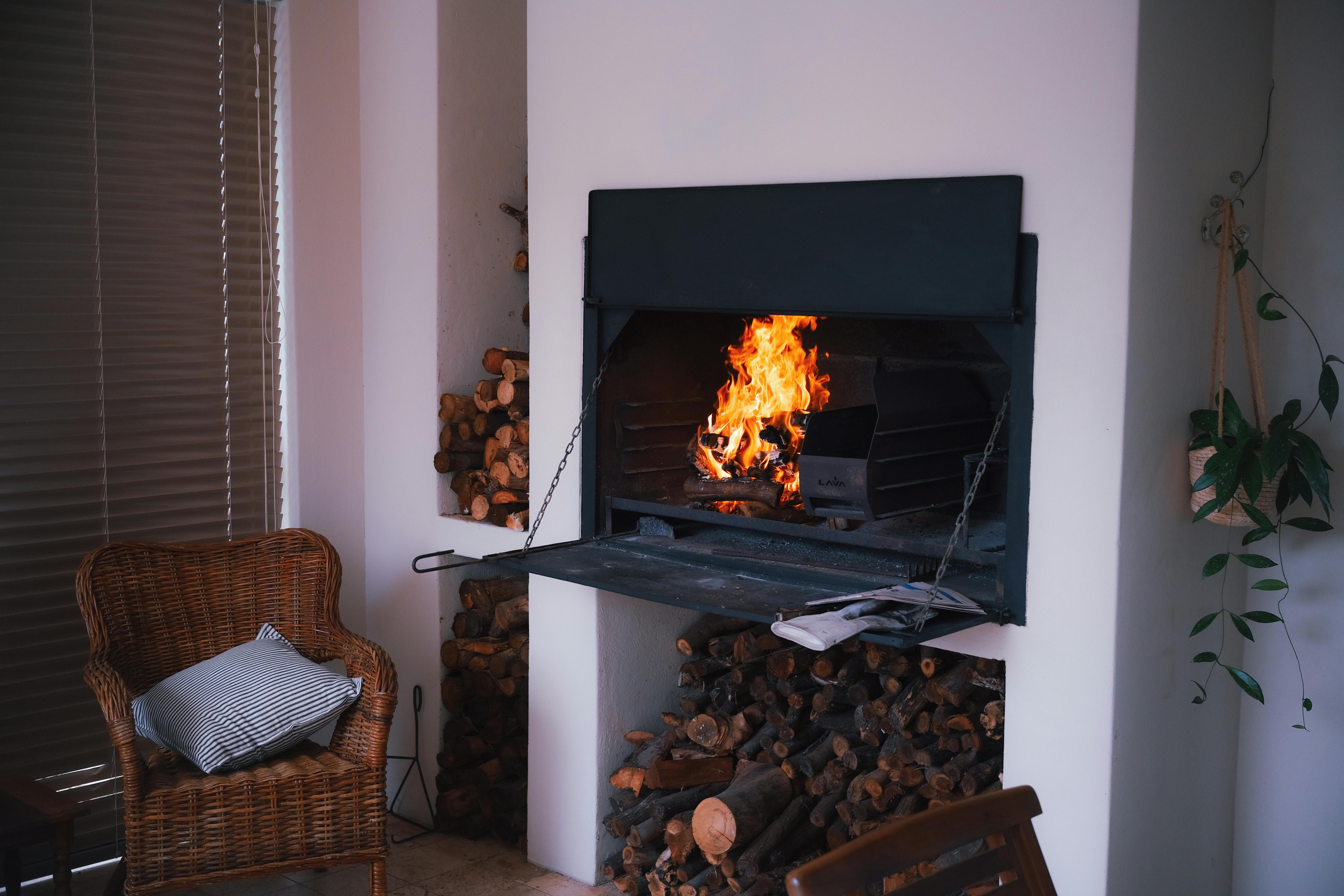 Une cheminée intérieure chaleureuse et accueillante avec du bois de chauffage empilé, un fauteuil en osier et des plantes pour une ambiance cosy.