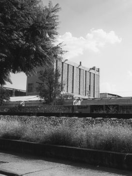 A black and white photo of an industrial building with surrounding greenery.