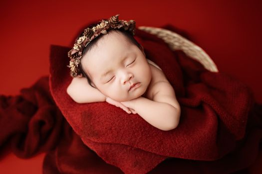 Cute newborn sleeping on red blanket with floral headband, perfect for holiday or family themes.