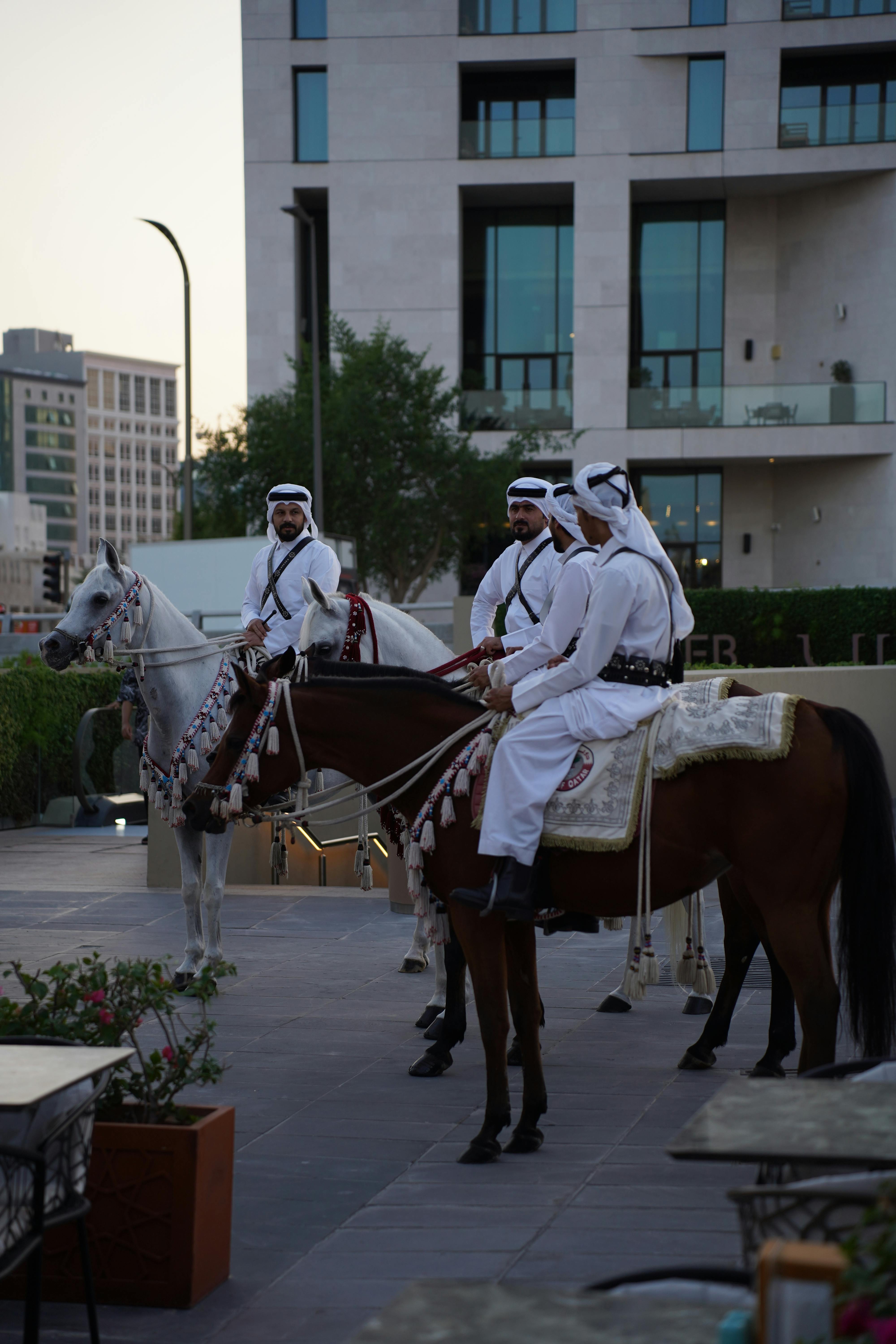 Qatari men in traditional attire on horseback amidst modern architecture.