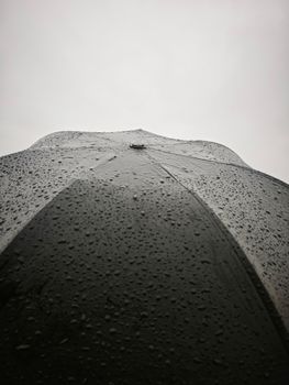 Detailed view of a black umbrella with raindrops against a grey sky, highlighting rainy weather.