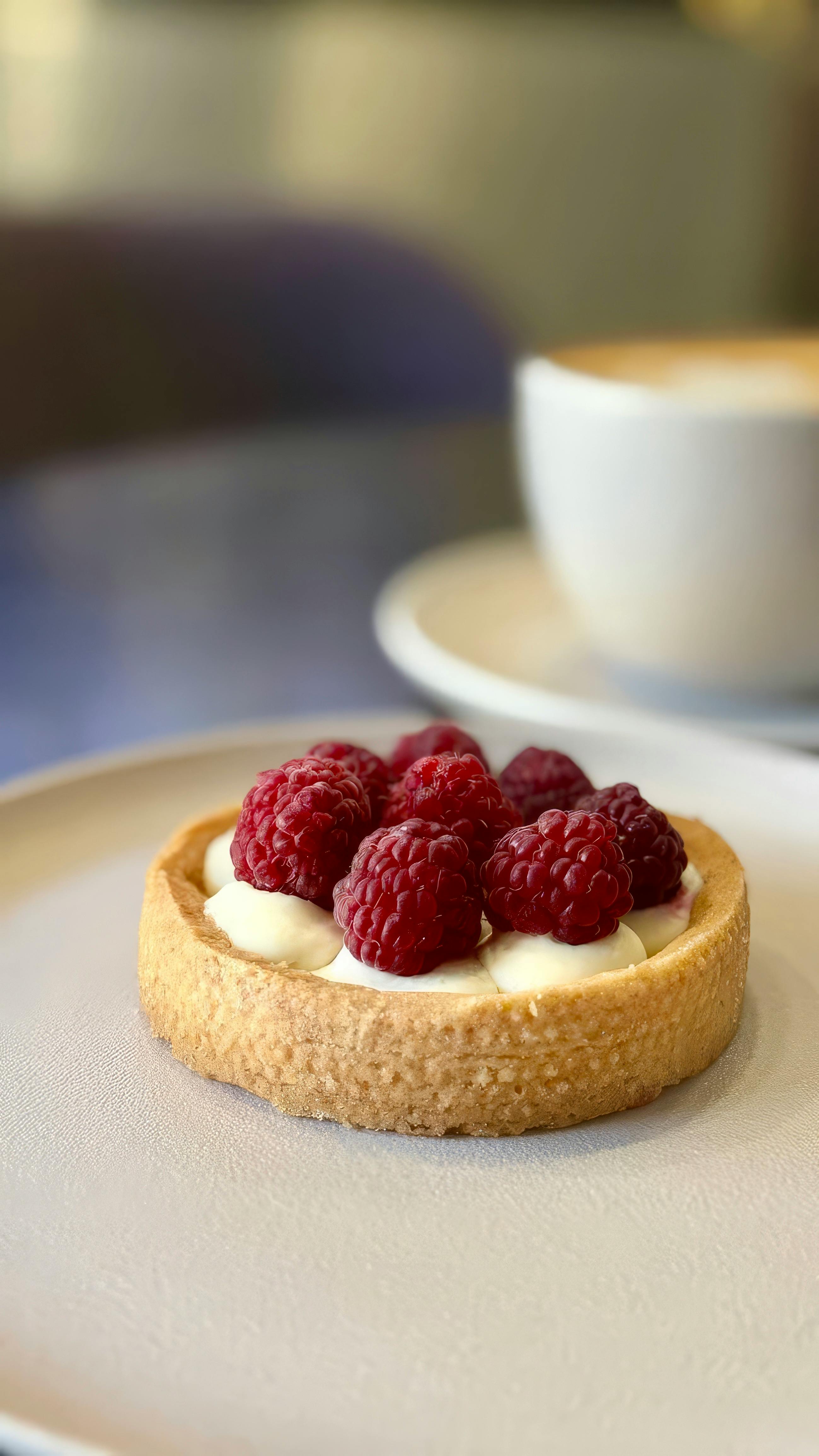 Close-up of a fresh raspberry tart with a cappuccino in a cozy café setting.
