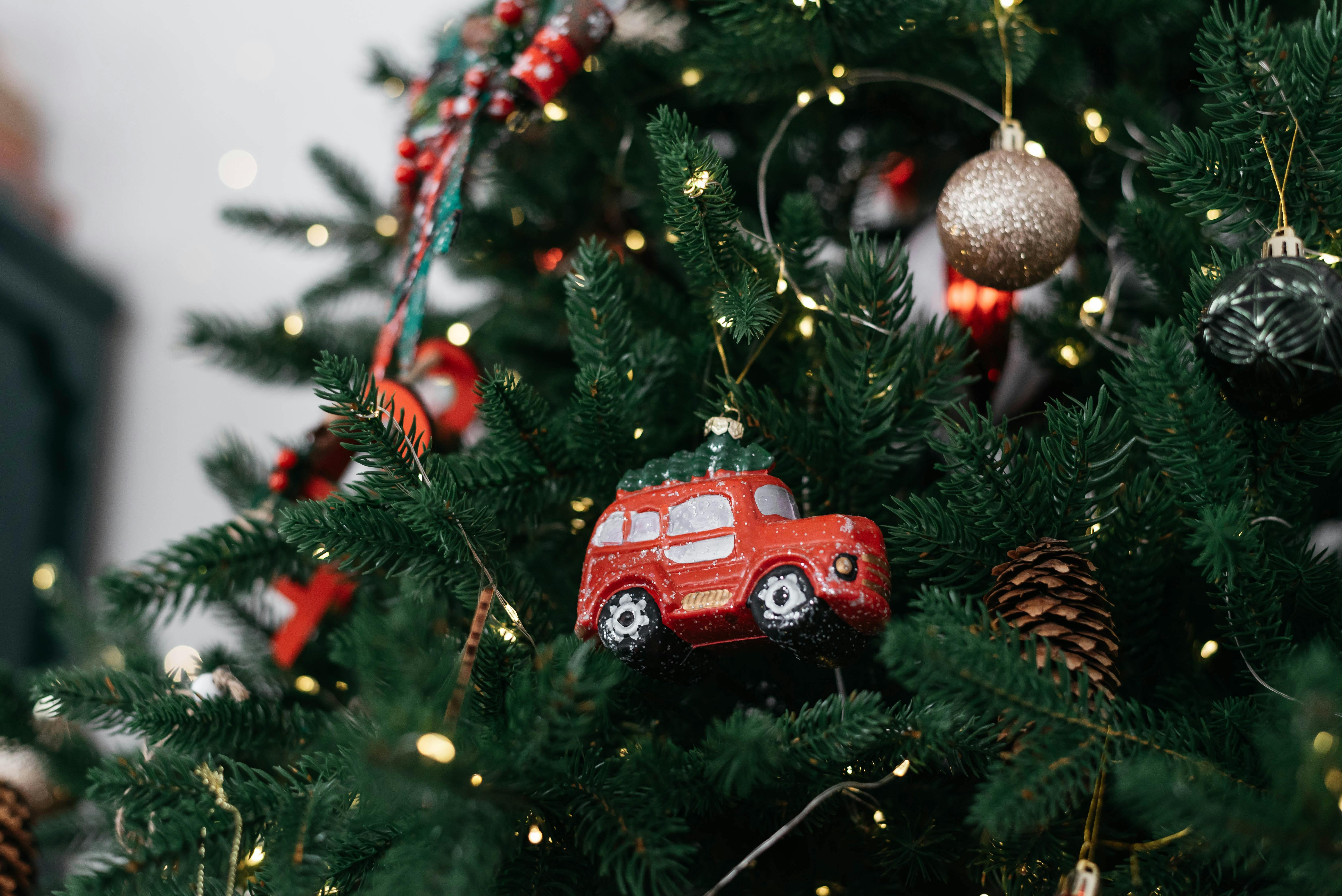 A close-up of a Christmas tree decorated with lights and a red car ornament.