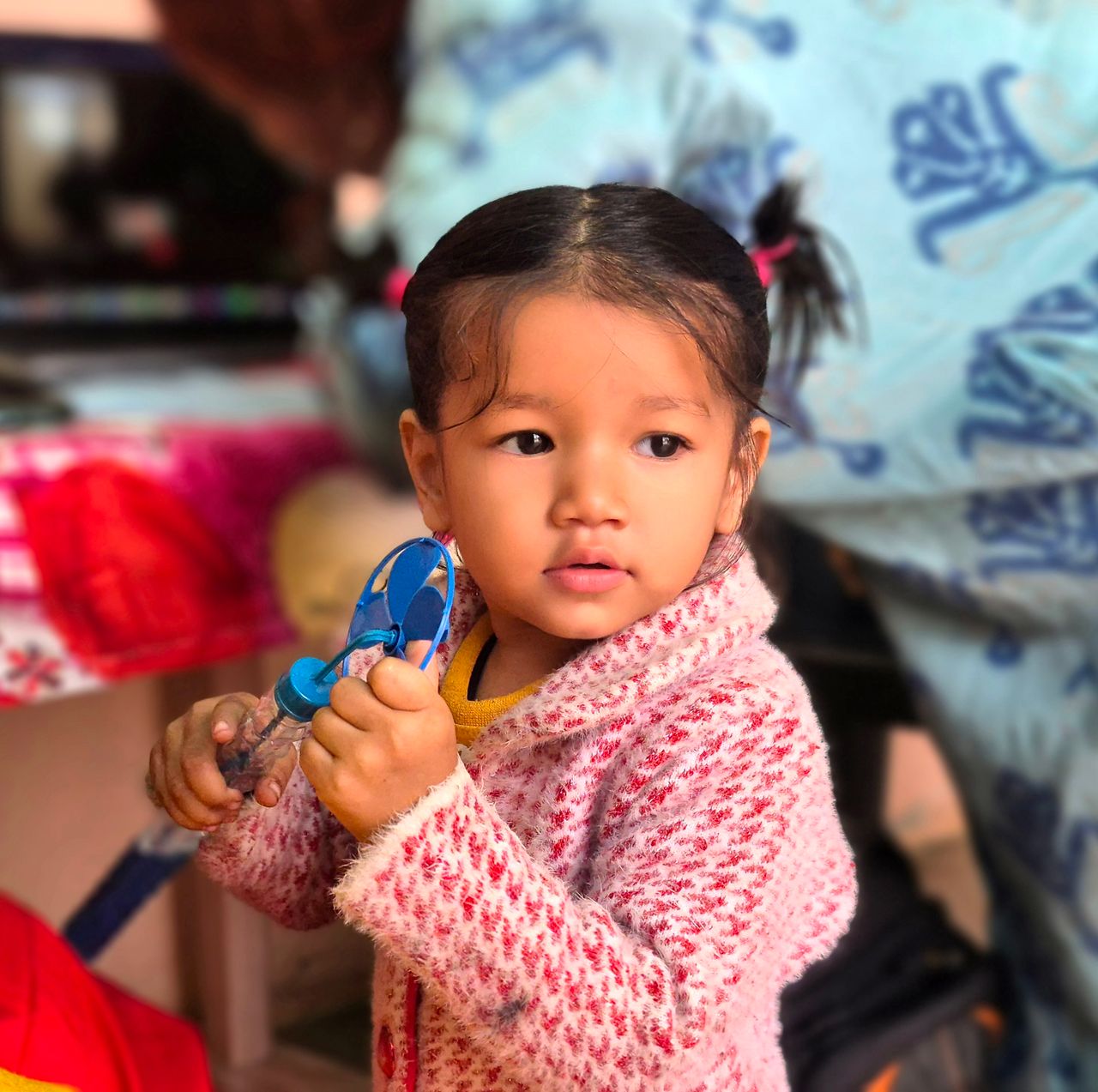 adorable girl in a pink sweater holds a toy with a soft focused backgr