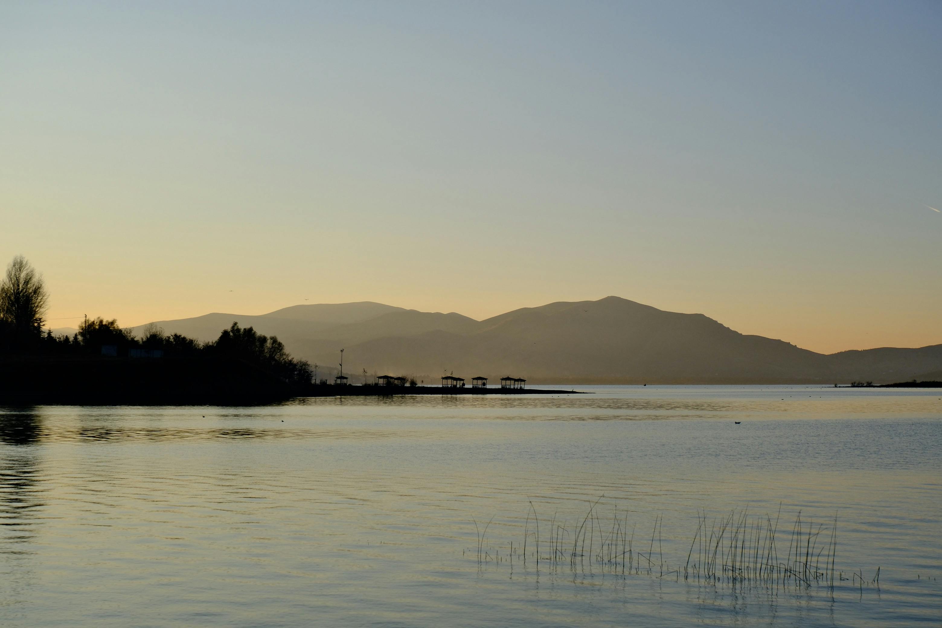 grátis Um pôr do sol tranquilo sobre um lago sereno com silhuetas de montanhas ao fundo. Foto profissional