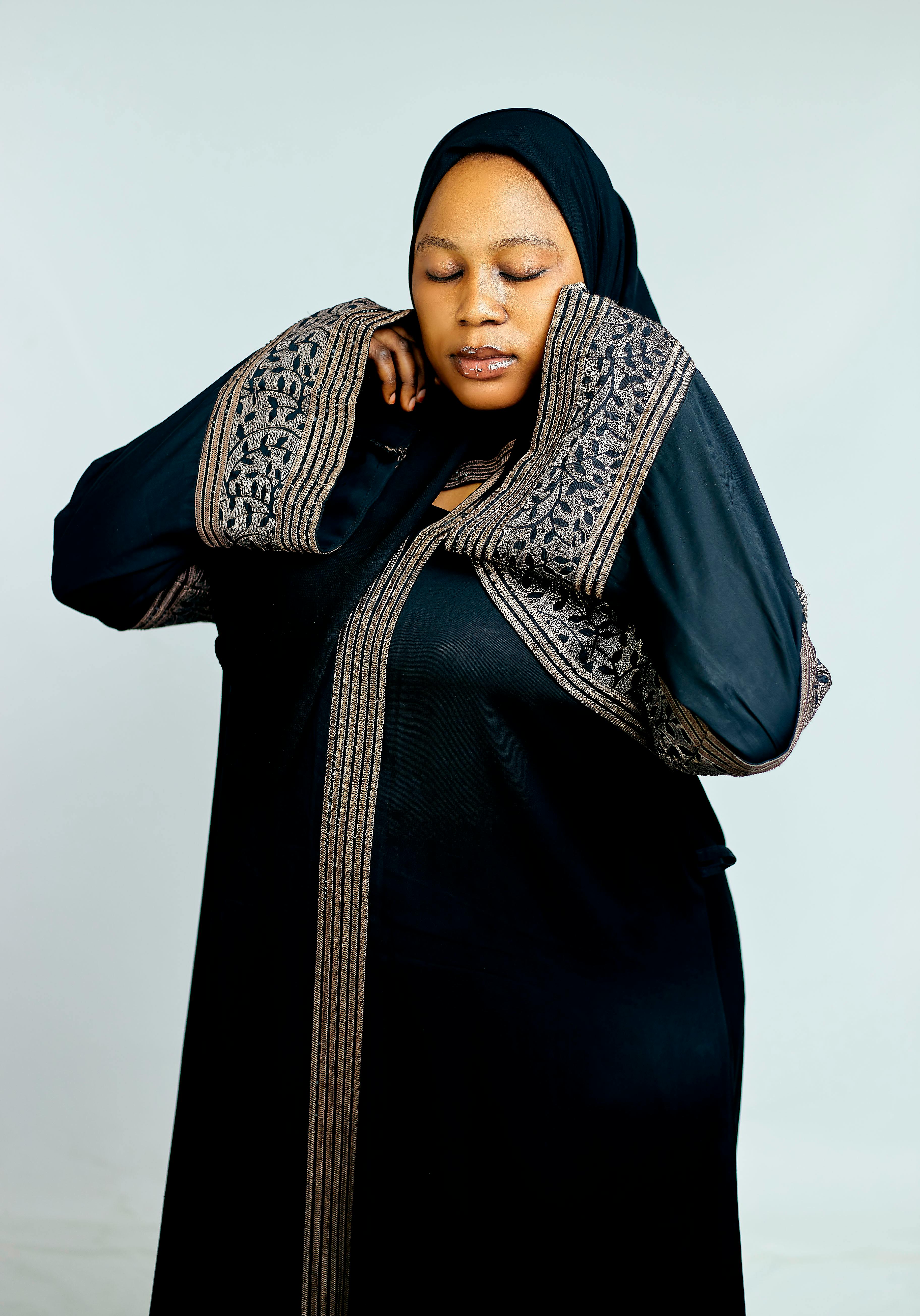 Middle Eastern woman wearing traditional black abaya, closed eyes in contemplation.