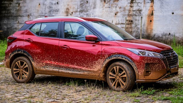 A red Nissan SUV with mud splatters seen parked on cobblestone.