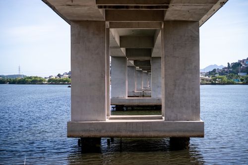 Free Symmetrical concrete bridge pillars create an endless pattern over calm water. Stock Photo