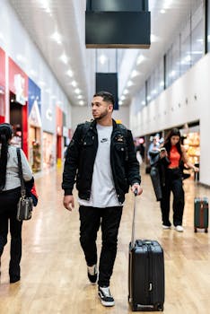 Casual man with suitcase walks through a bright airport terminal surrounded by travelers.