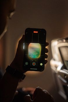 A person films outside the airplane window with a smartphone, capturing scenic views.