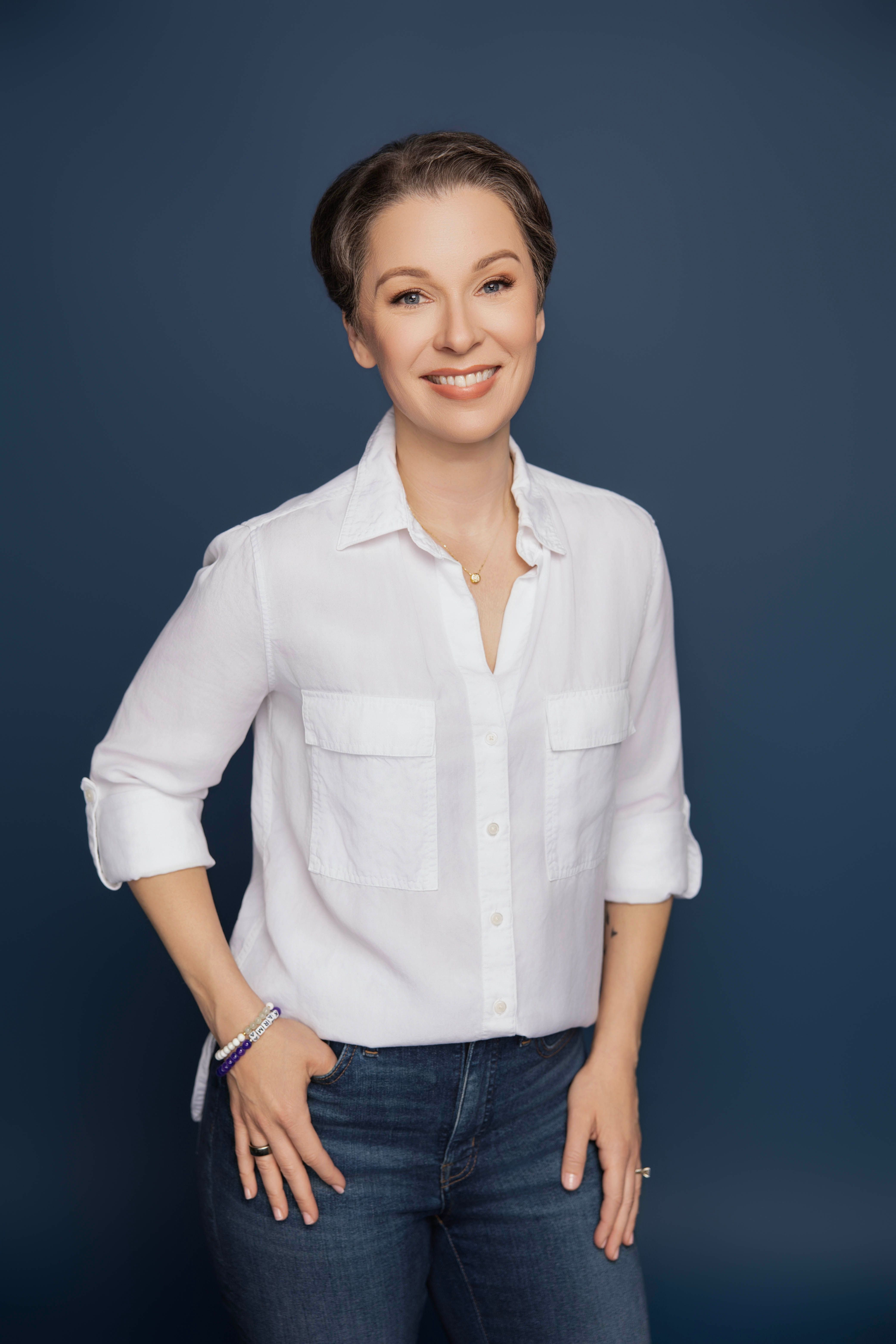 Smiling woman in casual white shirt and jeans against a blue background, exuding confidence.