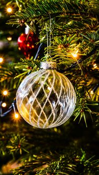 Close-up of a sparkling Christmas ornament hanging on a decorated evergreen tree with warm festive lights.