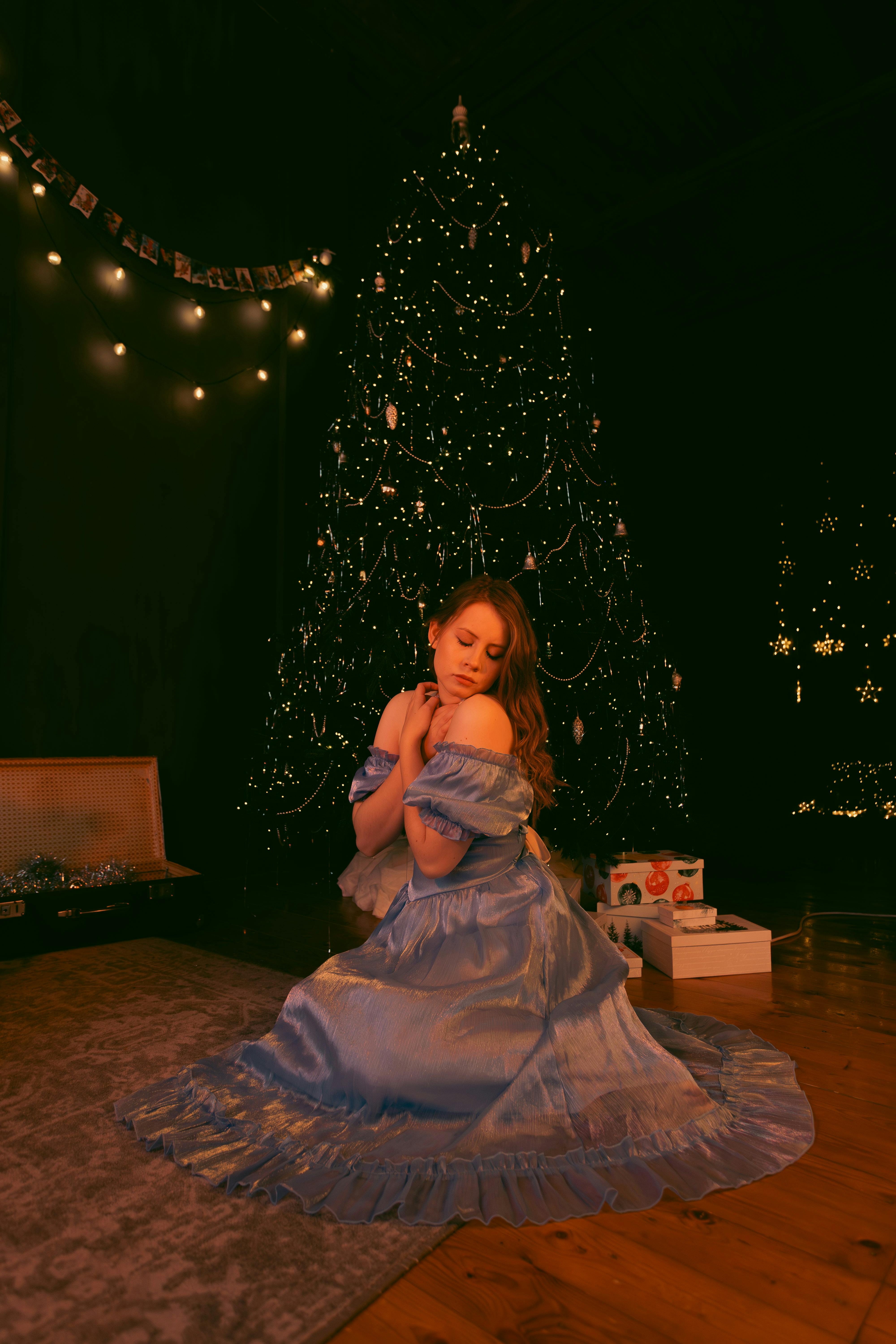 Woman in blue dress embracing holiday spirit by a sparkling Christmas tree.