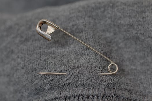 A detailed view of a safety pin resting on a textured gray fabric surface.