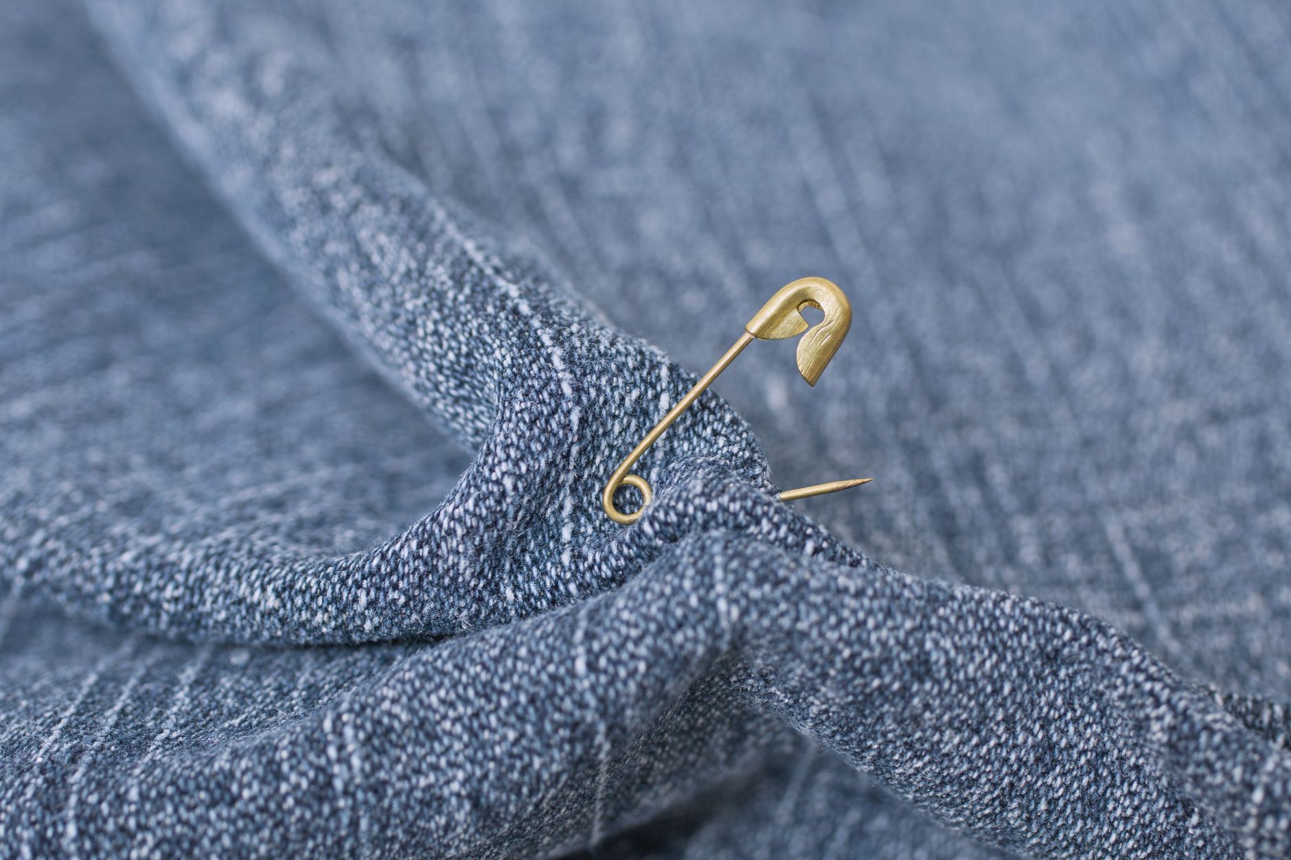 Detailed close-up of a safety pin attached to textured blue denim fabric.