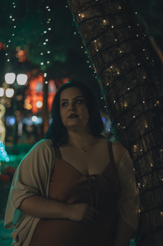 Woman standing by a tree wrapped in lights during the night.