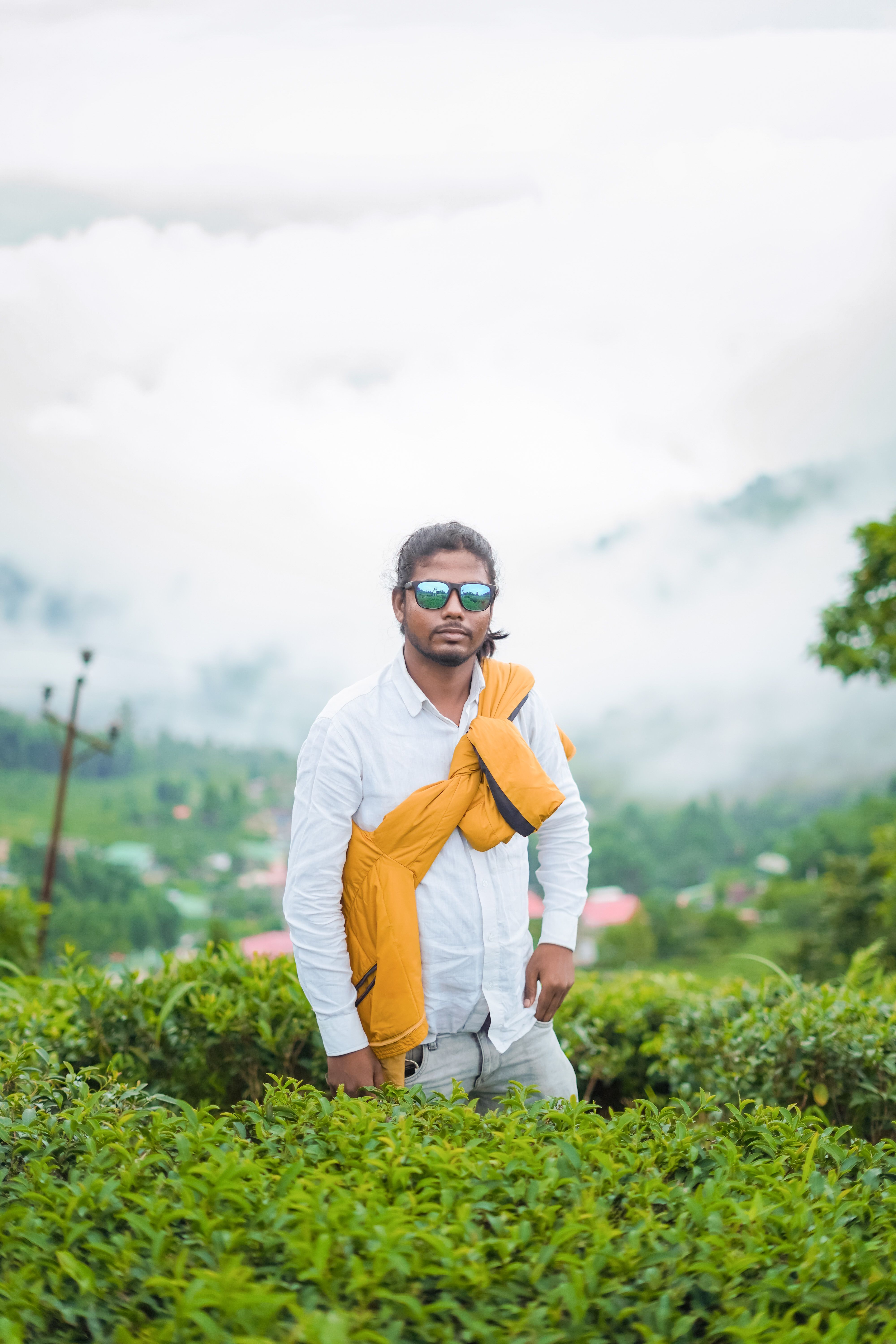 A man in sunglasses stands confidently in a lush, misty tea plantation, capturing serenity and adventure.
