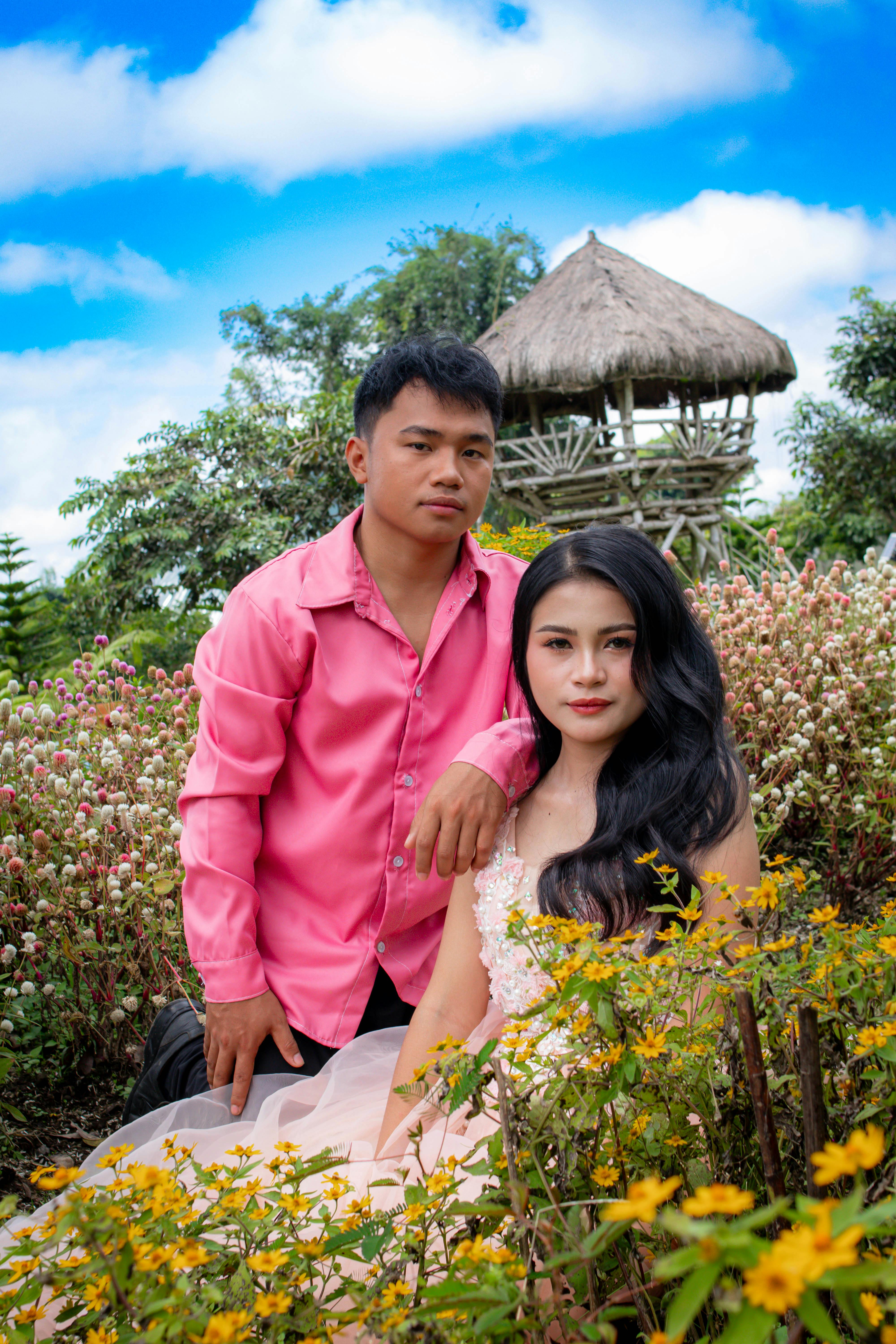 A young couple poses in a vibrant garden, surrounded by flowers and greenery.