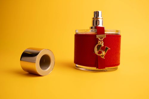 Free A stylish luxury perfume bottle with a red covering and gold accents against a bright yellow backdrop. Stock Photo