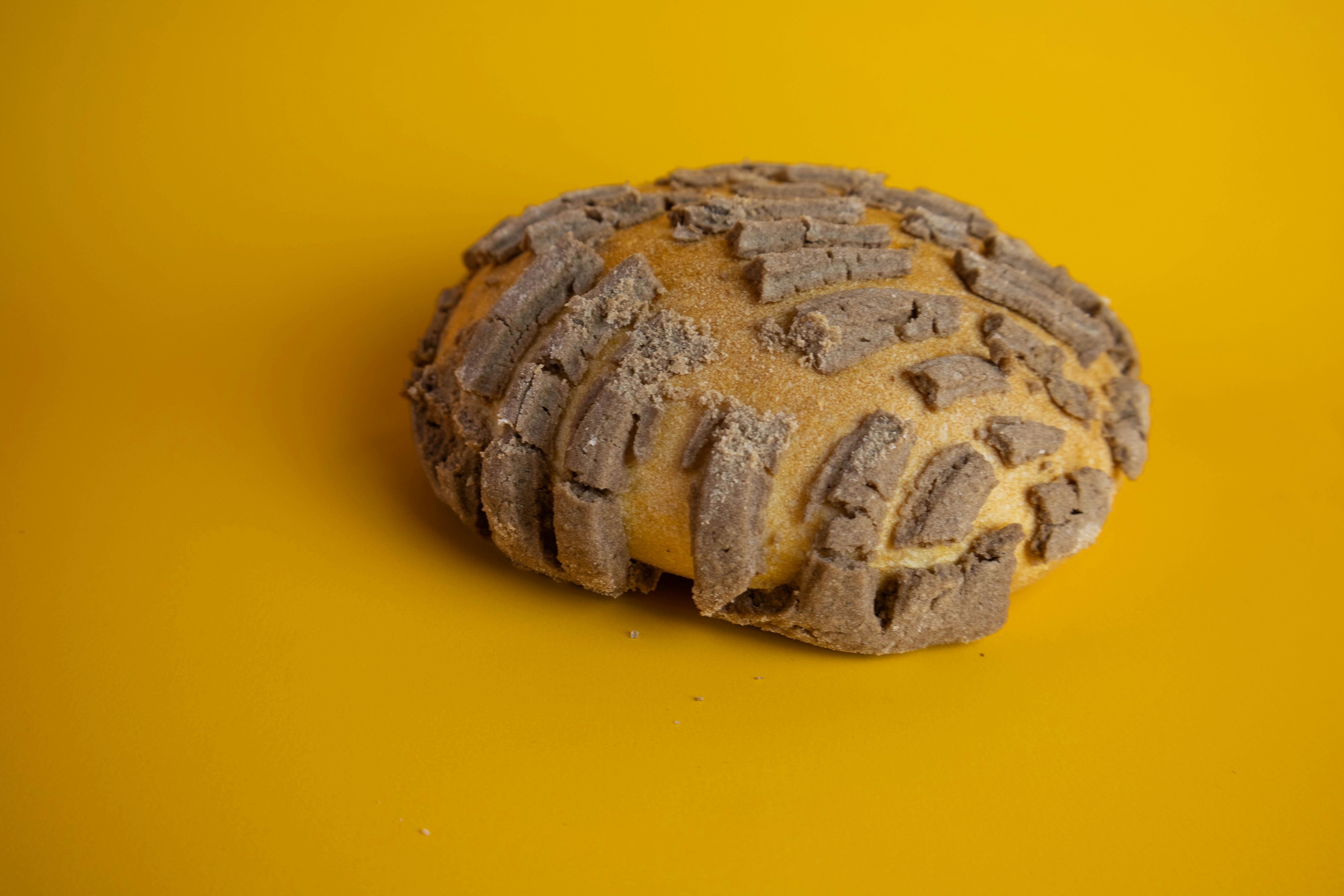 Close-up of a traditional concha bread with chocolate topping against a yellow backdrop.