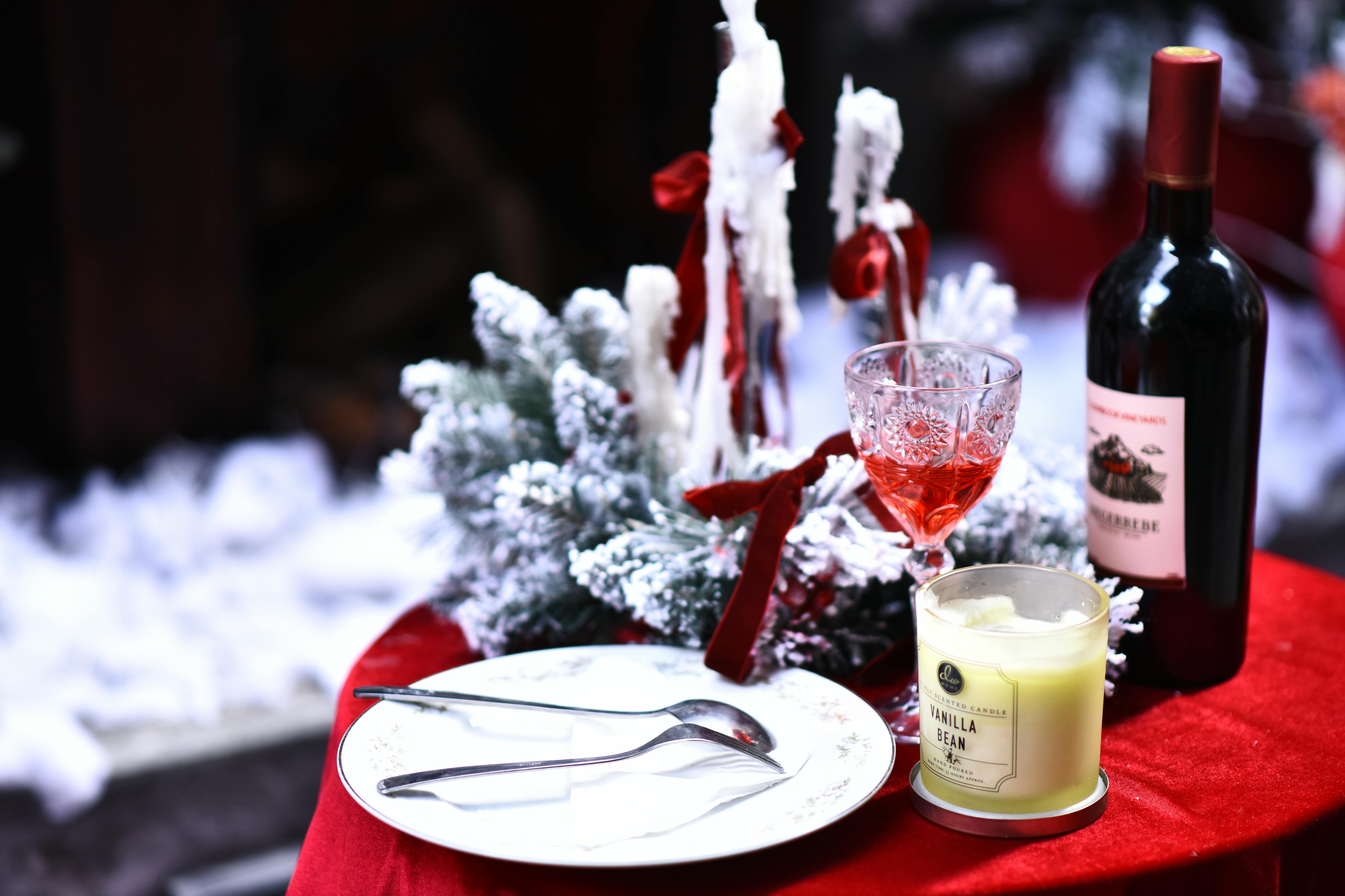 Cozy winter dinner setting featuring wine, candle, and snowy decor on a red tablecloth.