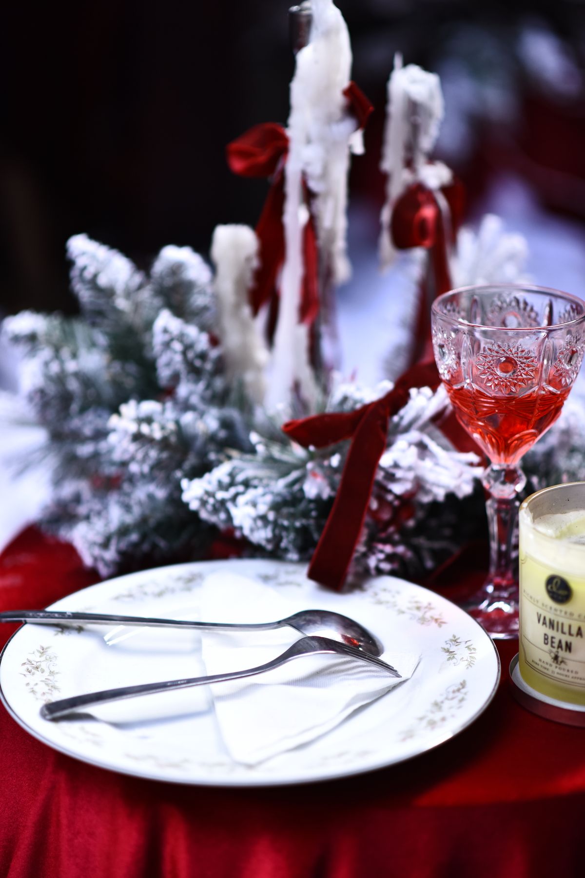 Holiday place setting with a white plate, polished cutlery, a wine glass and lit candles on a table set two days early