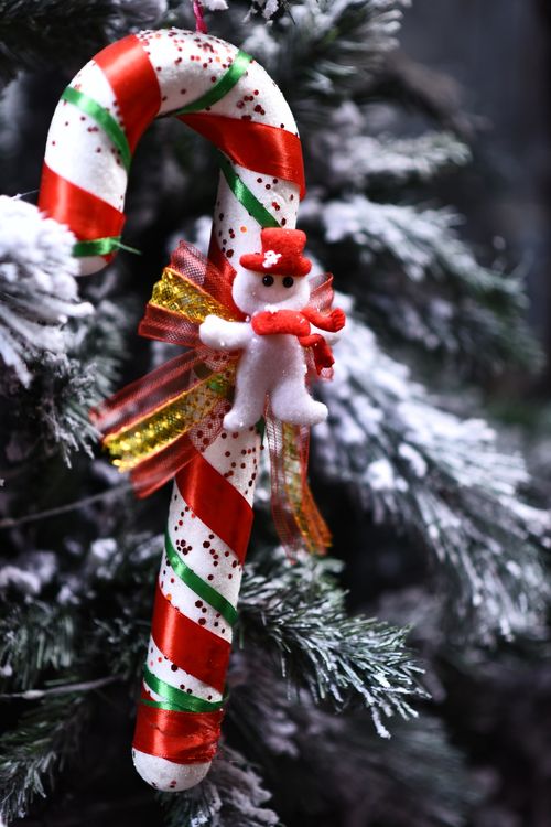 Free Colorful candy cane ornament with snowman on snow-covered Christmas tree branch. Stock Photo