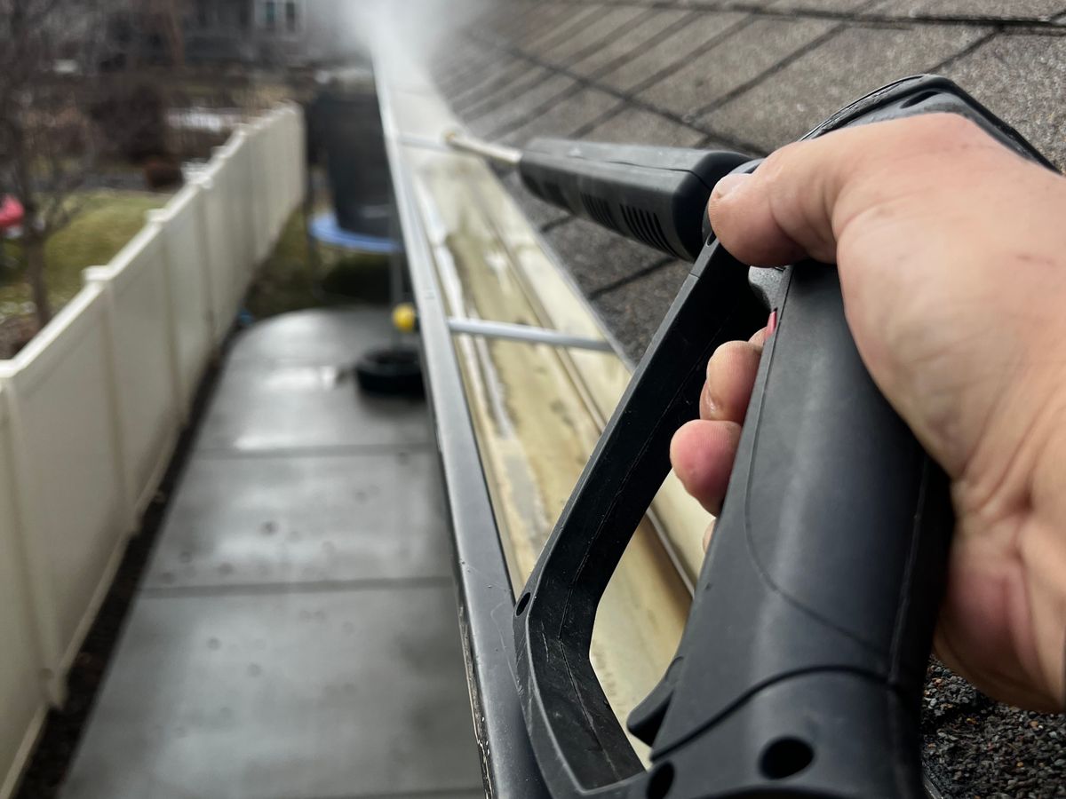 Close-up of a gutter being cleaned with a high pressure washer wand